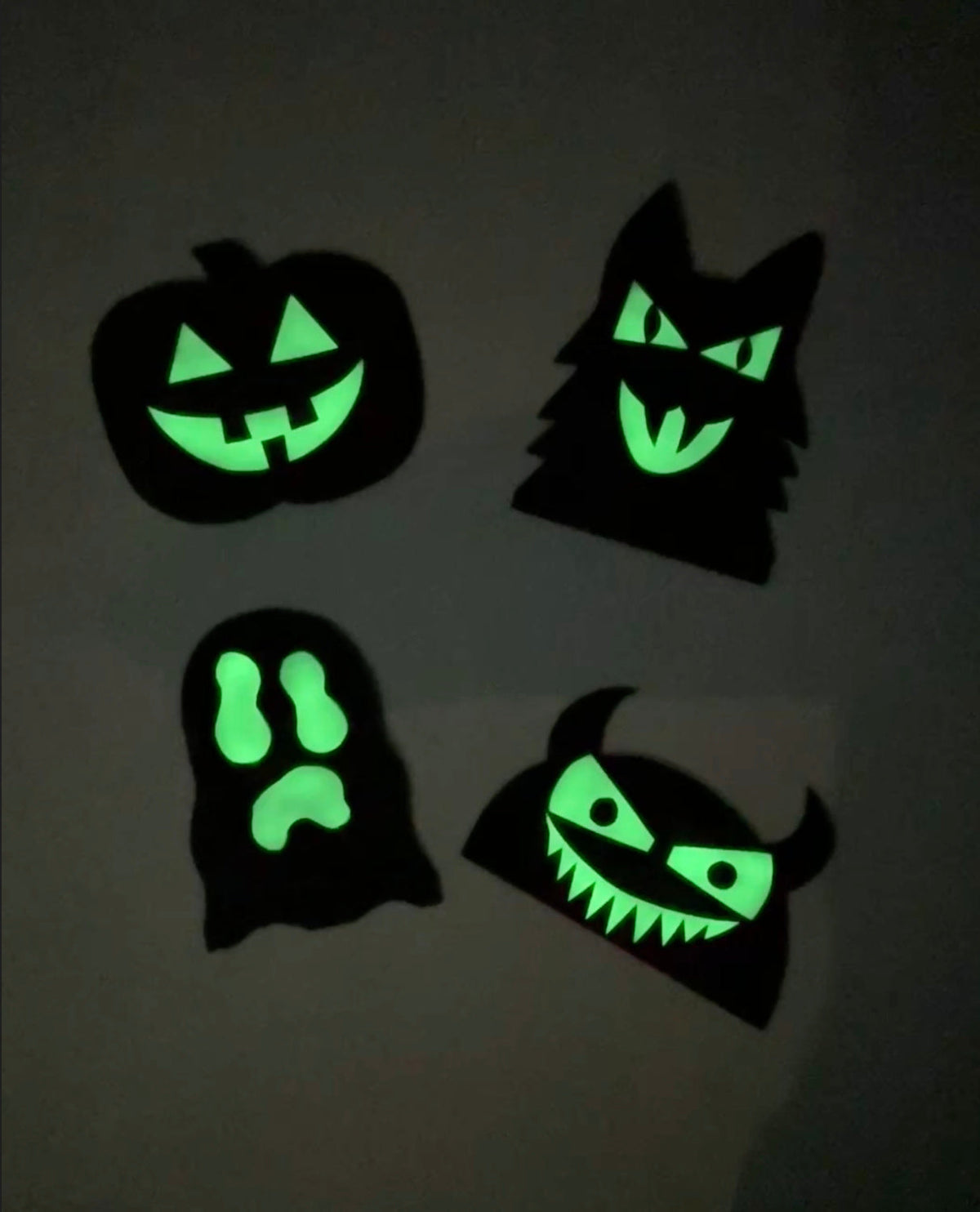 Four black Halloween shapes with glowing facial features, pumpkin, werewolf, ghost and devil.