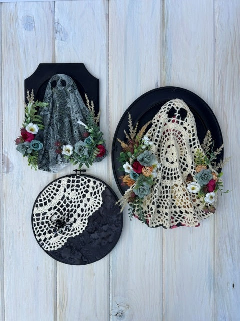 Three stiffened lace projects (2 ghosts, 1 spider) on black wood frames on whitewashed background